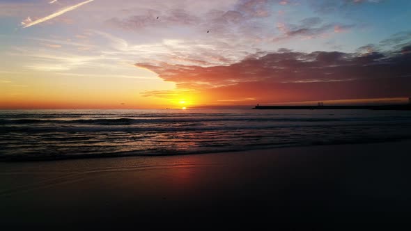 A drone flies down the coast revealing a stunning sunset at the beach