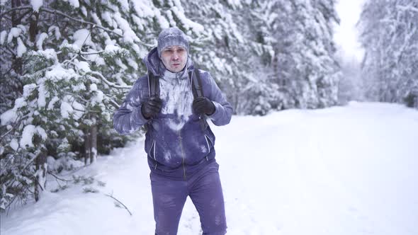 Stern Frozen Man in the Cold Winter Goes Through the Woods with a Backpack