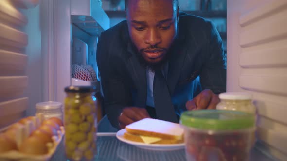 Businessman Taking Sandwich Out of Refrigerator in Kitchen at Night