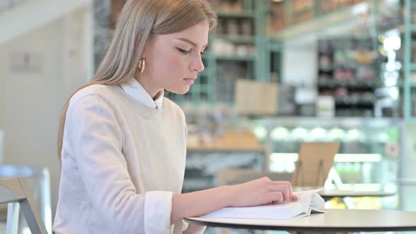 Studious Young Woman Reading Book in Cafe