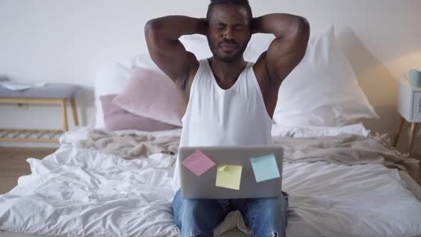 Camera Approaches to Young African American Man Typing on Laptop Keyboard and Falling Back on Bed