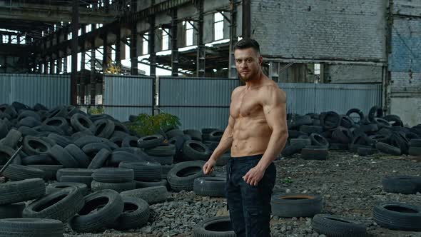 Handsome muscular man posing outside. Muscular man standing against old tyres background