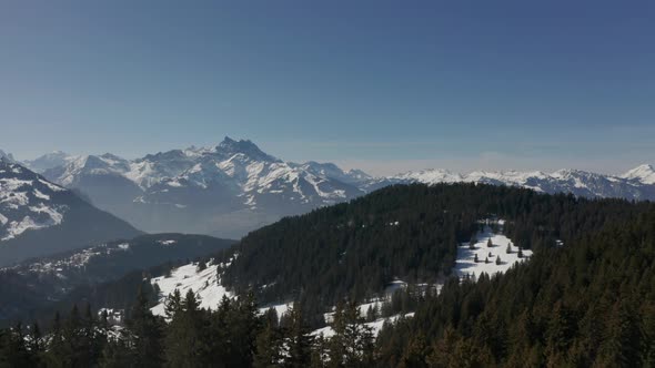 Aerial of beautiful snow covered valley with green forests. Drone flying backwards