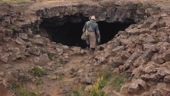 Man In Long Coat With Guitar Case Walking Into Cave