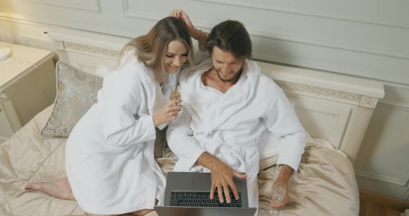 Young Tourists Couple Are Browsing the Internet at Laptop Together Sitting on a Bed in a Hotel Room