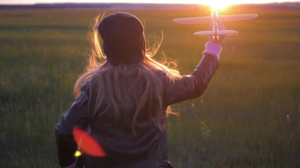 Happy Little Girl Playing with an Airplane in the Meadow During Sunset