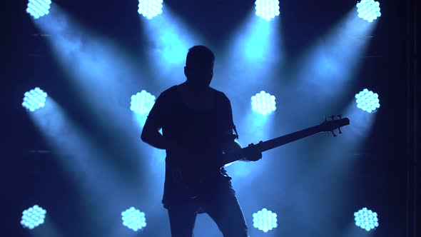 Silhouette of a Young Guy Playing on the Electric Guitar on Stage in a Dark Studio with Smoke and