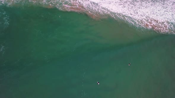 Surfers waiting to catch a wave, one failed attempt. Birds-eye-view drone-shot.