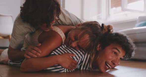 Three young adults laughing together and laying on top of each other on the floor