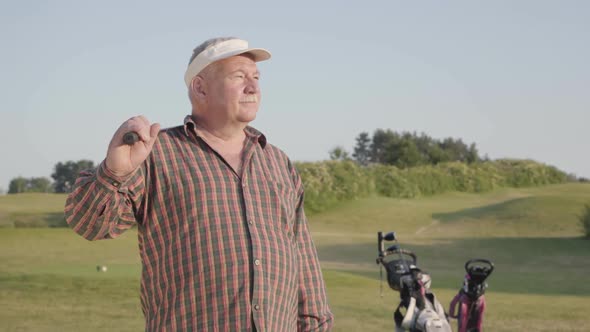 Portrait of a Confident Successful Mature Man with a Golf Club Standing on a Golf Course