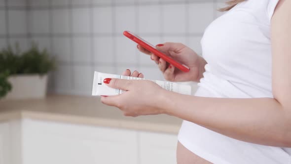 Pregnant Woman Hands with Smartphone Reading Label on a Bottle