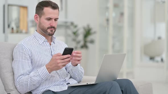 Hardworking Young Man Using Smartphone and Laptop at Home