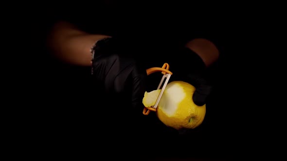 Person Cuts Zest From Lemon with Peeler on Black Background