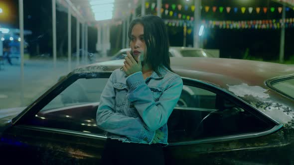 A Girl Smokes in Front of a Rusty Classic Car While Typing a Message Late at Night