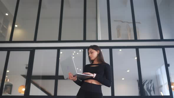 Young Woman Holding Laptop in Hands and Browsing Internet at Home