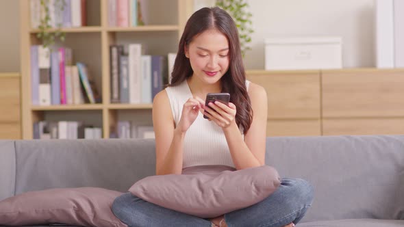 Millennial asian young woman looking mobile phone laughing with good news or discount voucher for sh