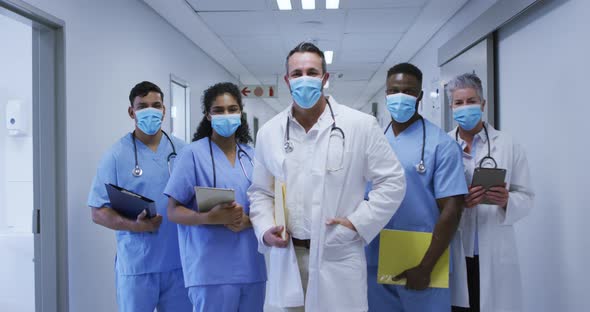 Portrait of diverse group of male and female doctors in face masks standing in hospital corridor