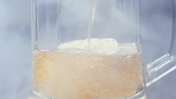 Close Up View of Beer Is Pouring From the Bottle Into Glass with Cold Smoke in Background in