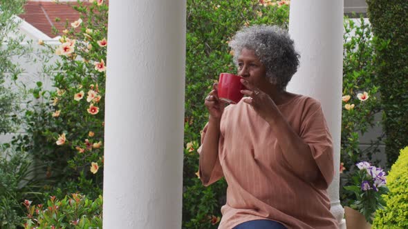 Senior african american woman drinking coffee while sitting on the porch of the house