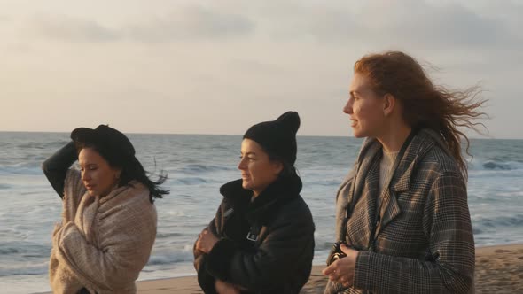 Three Beautiful Young Women Walking on the Sand Beach at Sunset or Sunrise