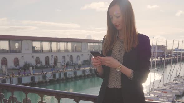 Young Woman with Smartphone at Yacht Port at Spa Resort.