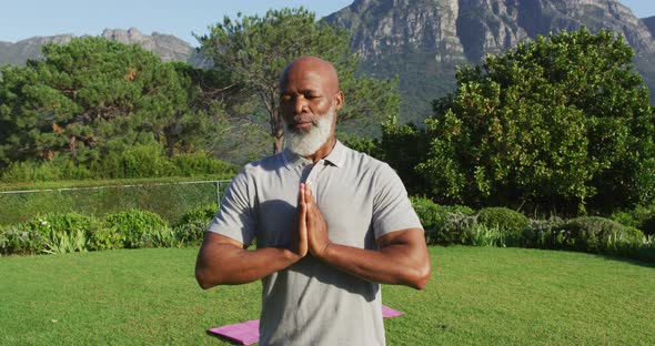 African american senior man practicing yoga and meditating in the garden