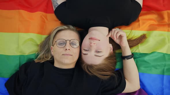 Pretty LGBT Couple Lying on Rainbow Flag and Looking at you