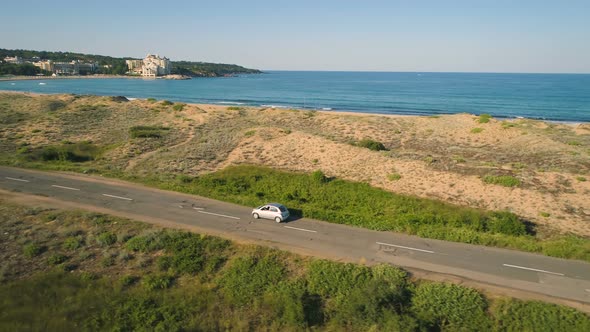 Silver Car Driving Along Coast in Alepu, Bulgaria, Drone Follows Car Driving Slowly Near Beach