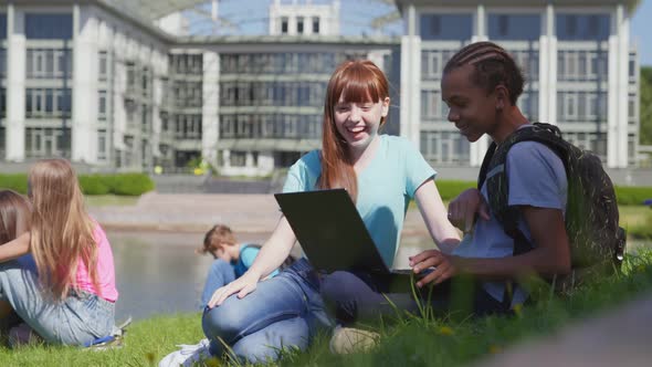 Diverse Schoolchildren Enjoying Break on Green Lawn Using Laptop