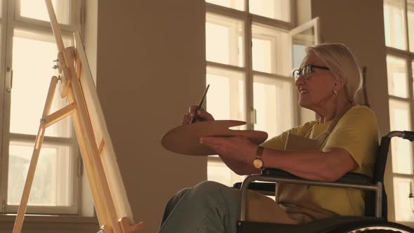 An Elderly Woman with a Disability Paints a Picture While Sitting in a Wheelchair