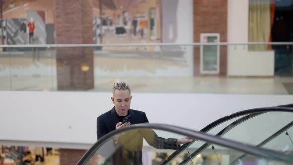 Cute Stylish Homosexual Man in a Shopping Mall Climbs the Escalator