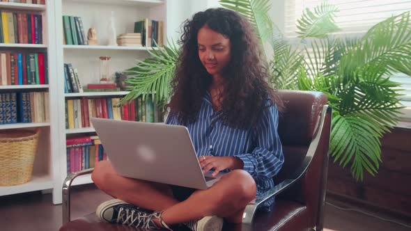 Young Modern Indian Woman Sitting in Chair and Working at Home Using Laptop