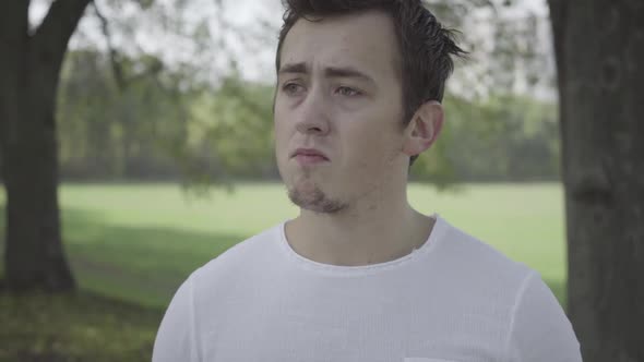 Closeup Portrait of Depressed Young Caucasian Man Standing in Summer Park Outdoors