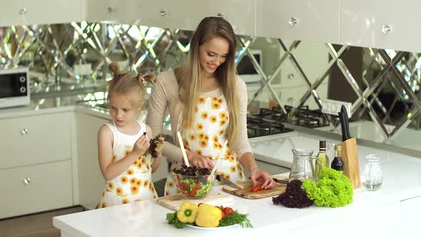 Mother With Daughter Cooking Vegetable Salad In Kitchen At Home