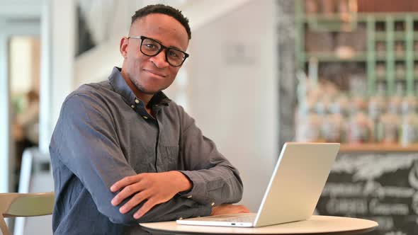 African Man with Laptop Looking at Camera in Cafe 