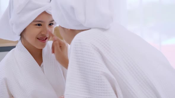 Mother with little daughter in bathrobes doing beauty treatment together at home.