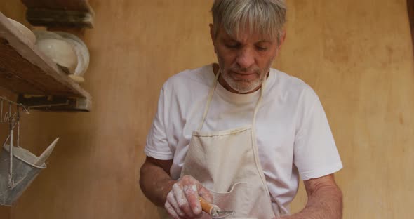 Senior caucasian man wearing apron using potter's wheel in pottery workshop