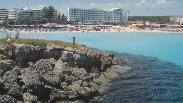 Zoom Out Aerial of Female Travel Blogger on Sea Coast on Tropical Resort in Ayia Napa in Cyprus