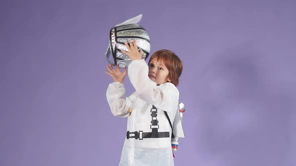 Beautiful Child Dressed in a White Spaceman's Suit and Tossing His Helmet in the Air