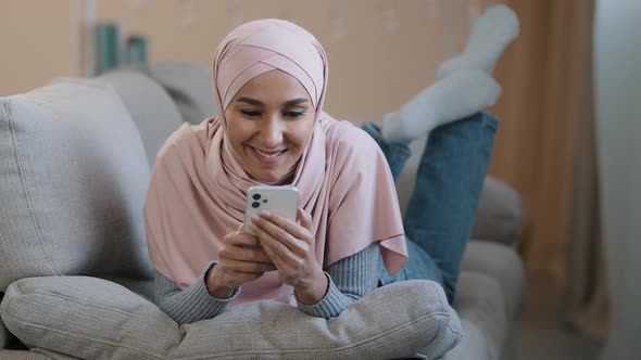 Young Attractive Arabian Muslim Girl Islamic Woman Lying on Home Sofa Happy Lebanese Lady Wear Hijab