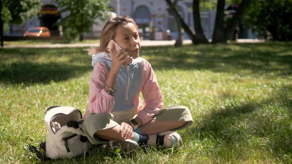 Beautiful Little Girl Is Talking on a Phone and Lying on a Green, Grass on a Sunny Summer Day