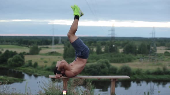 A Young Bodybuilder with a Naked Torso in Bright Sneakers Trains in Nature and Shakes His Abs While