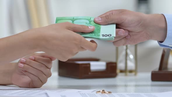 Male Giving Euros to Ex-Wife, Engagement Rings on Table, Alimony After Divorce