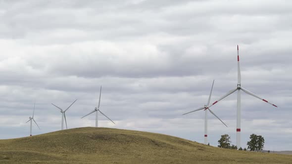 Motion the Blades of a Large Wind Turbine in a Field Against a Background of Cloudy Grey Sky on the