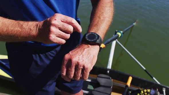 Senior caucasian man standing by a river checking smartwatch