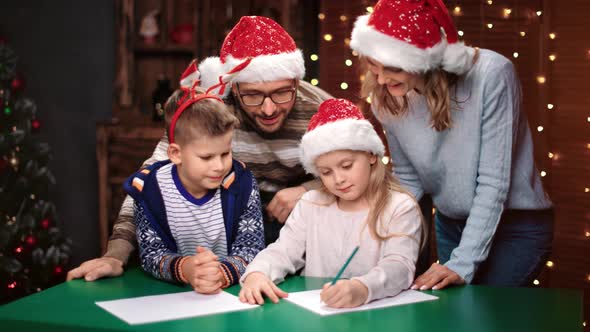 Boy and Girl Writing Wish List with Parents at Christmas Tree