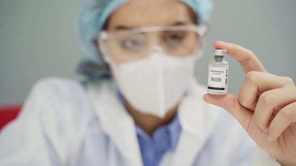 Asian female researcher doctor in PPE suit holding the COVID vaccine on laboratory during pandemic.