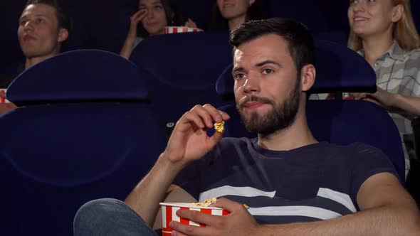 Attractive Young Man Eating Popcorn During Boring Movie at the Cinema