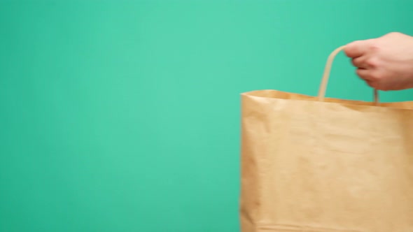 Courier in Gloves Passing Craft Shopping Bag with Delivery Against Mint Background