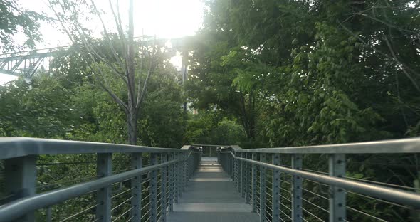 POV walking down a bridge on a path in a park